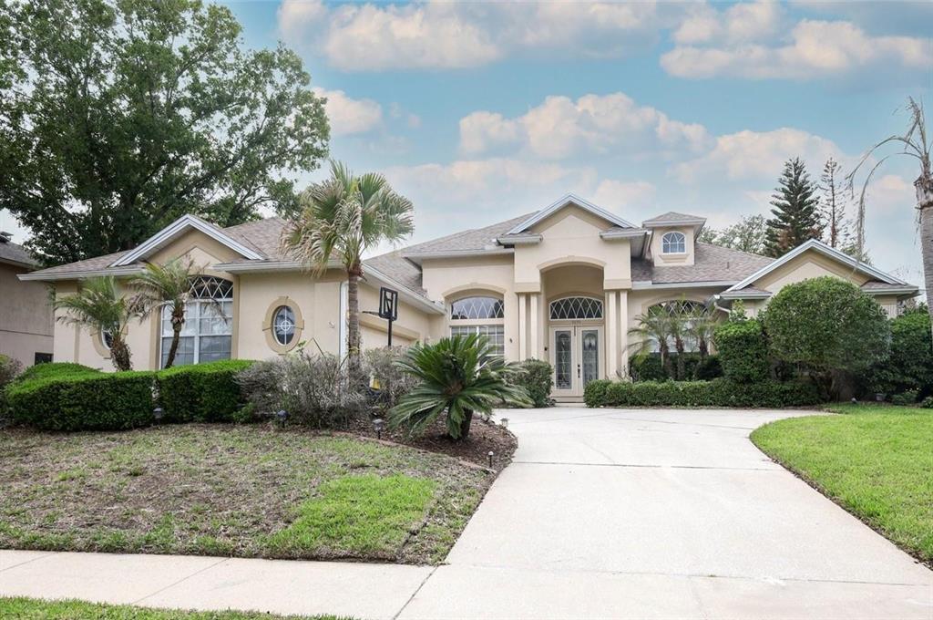 A single-story beige house with a concrete driveway, arched windows, and a landscaped front yard — 5695 POND PINE POINT, OVIEDO, FL