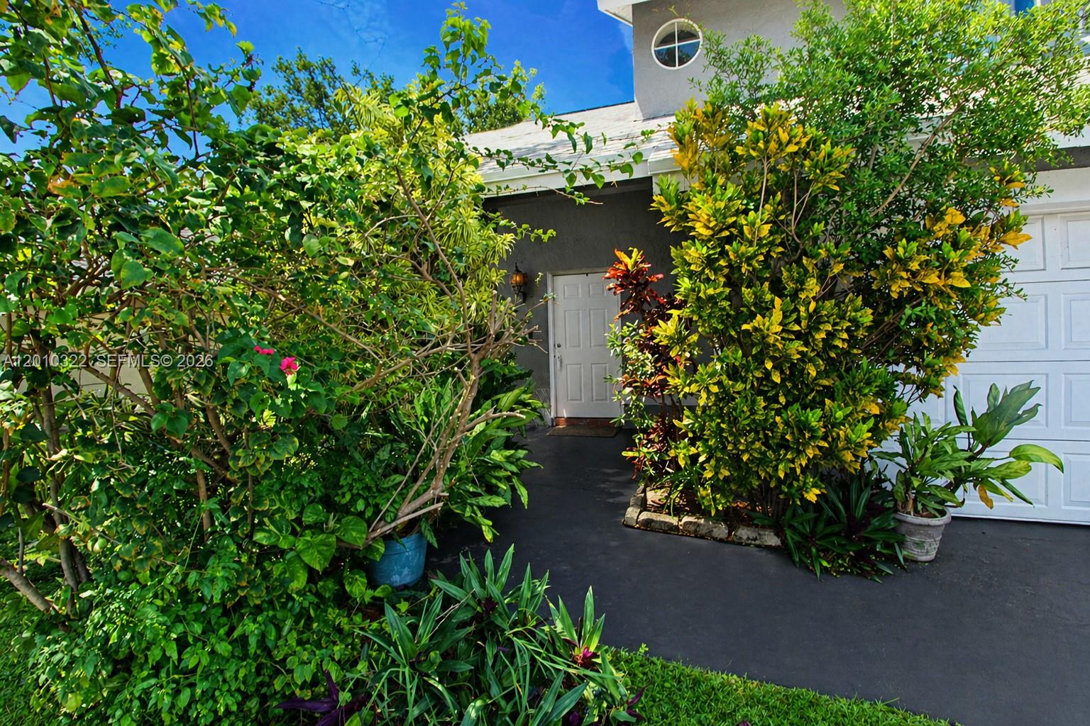 A white front door is nestled between lush green and yellow landscaping near a garage — 12113 NW 33rd St, Sunrise FL 33323, SUNRISE, FL