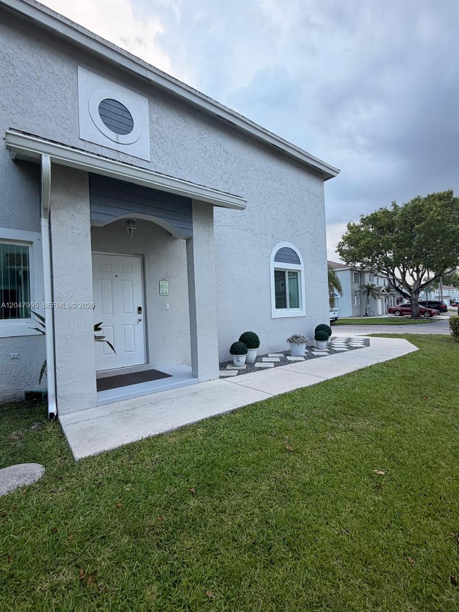 The exterior of a light-colored house features a covered entryway, a circular window, and landscaping — 1428 SW 47th Ave, Deerfield Beach FL 33442, DEERFIELD BEACH, FL