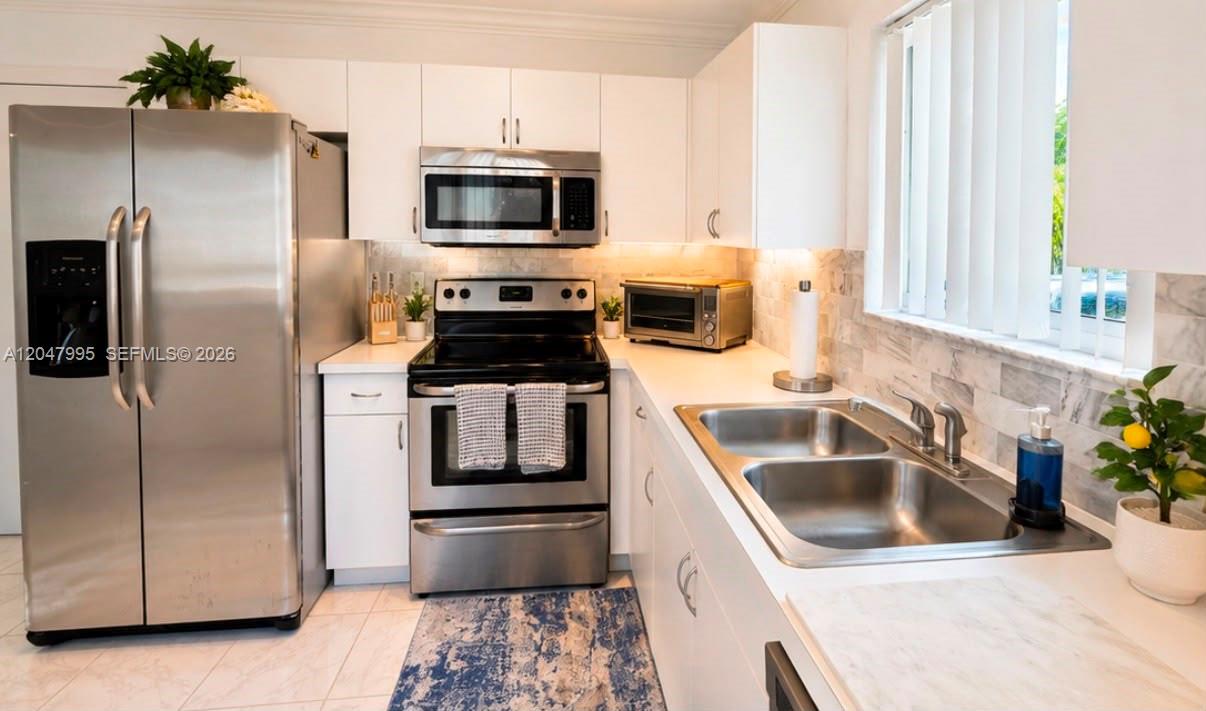 A kitchen features white cabinetry, stainless steel appliances, and a marble-patterned backsplash — 1428 SW 47th Ave, Deerfield Beach FL 33442, DEERFIELD BEACH, FL