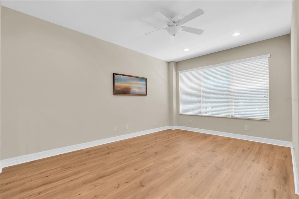An empty room with light wood-look flooring, beige walls, a ceiling fan, and large windows — 12670 SILVERDALE STREET, TAMPA, FL