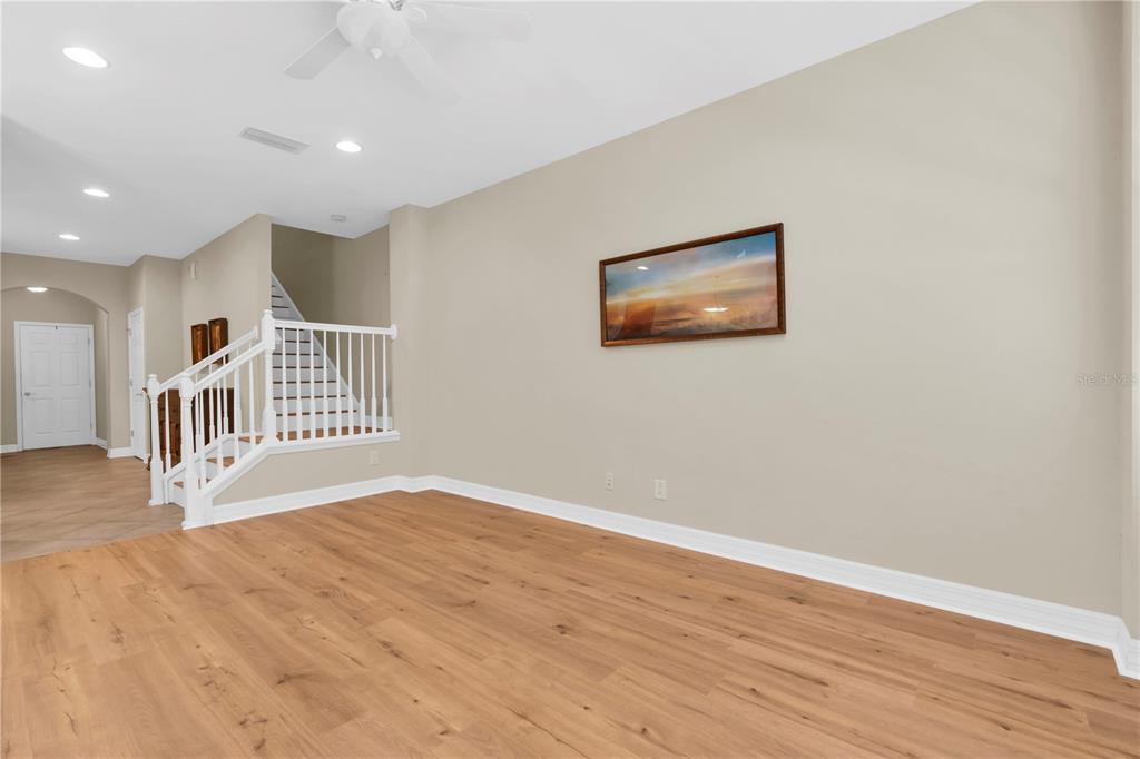 A living room with light wood-look flooring, beige walls, and a staircase with white railings — 12670 SILVERDALE STREET, TAMPA, FL