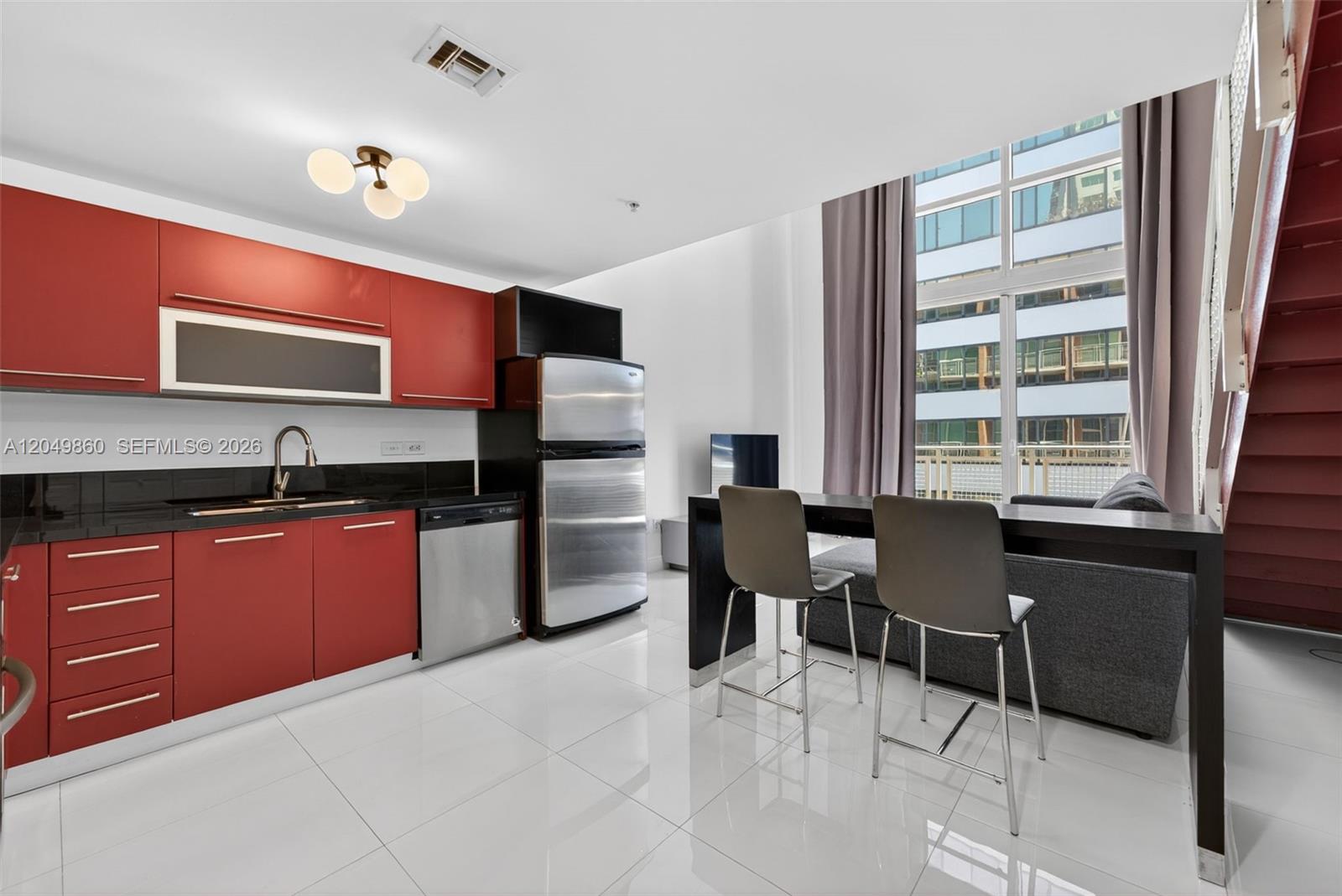 A modern kitchen with red cabinets and stainless appliances opens to a living area — 253 NE 2nd St # 424, Miami FL 33132, MIAMI, FL