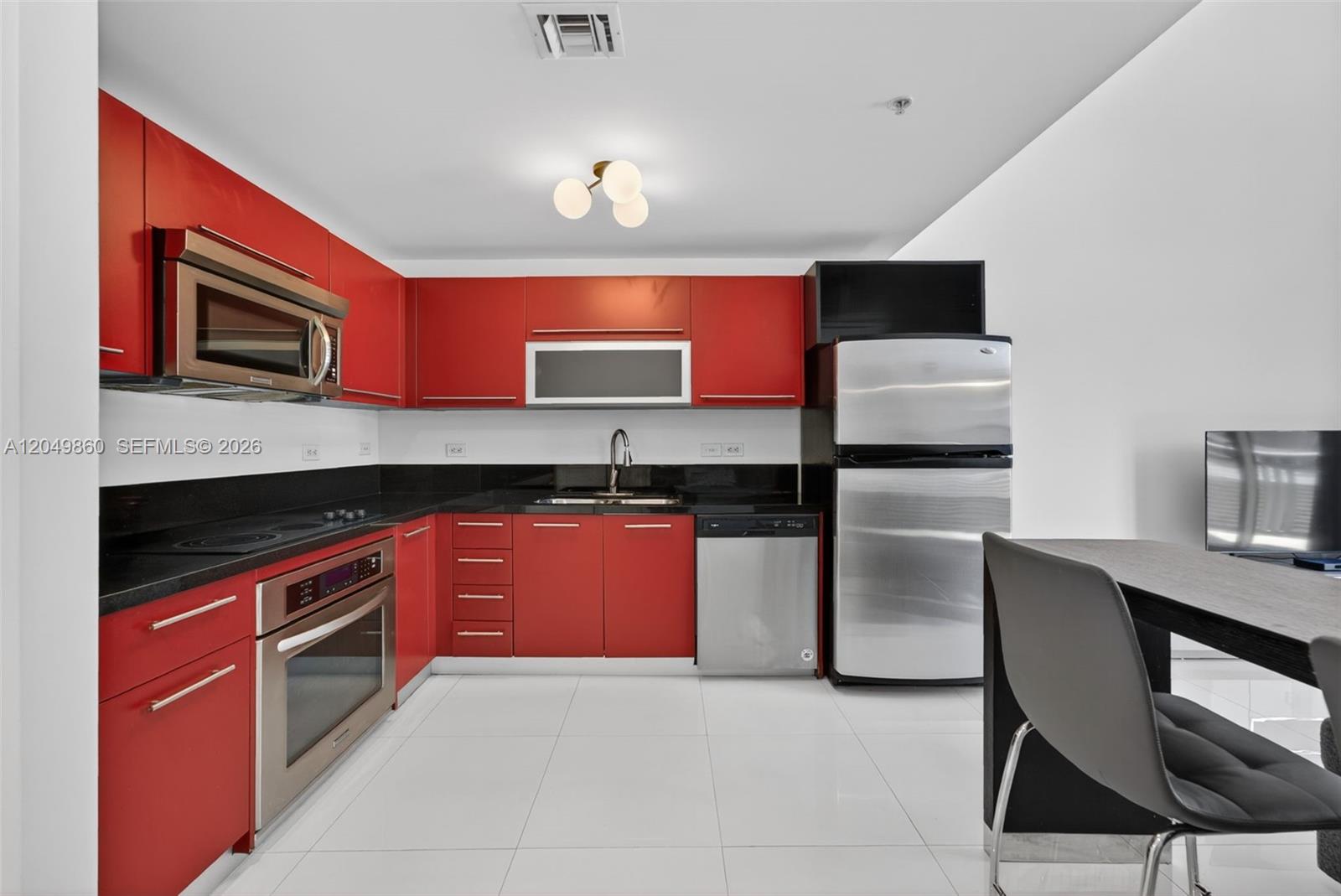 A kitchen features red cabinets, stainless steel appliances, and black countertops on white tile floors — 253 NE 2nd St # 424, Miami FL 33132, MIAMI, FL