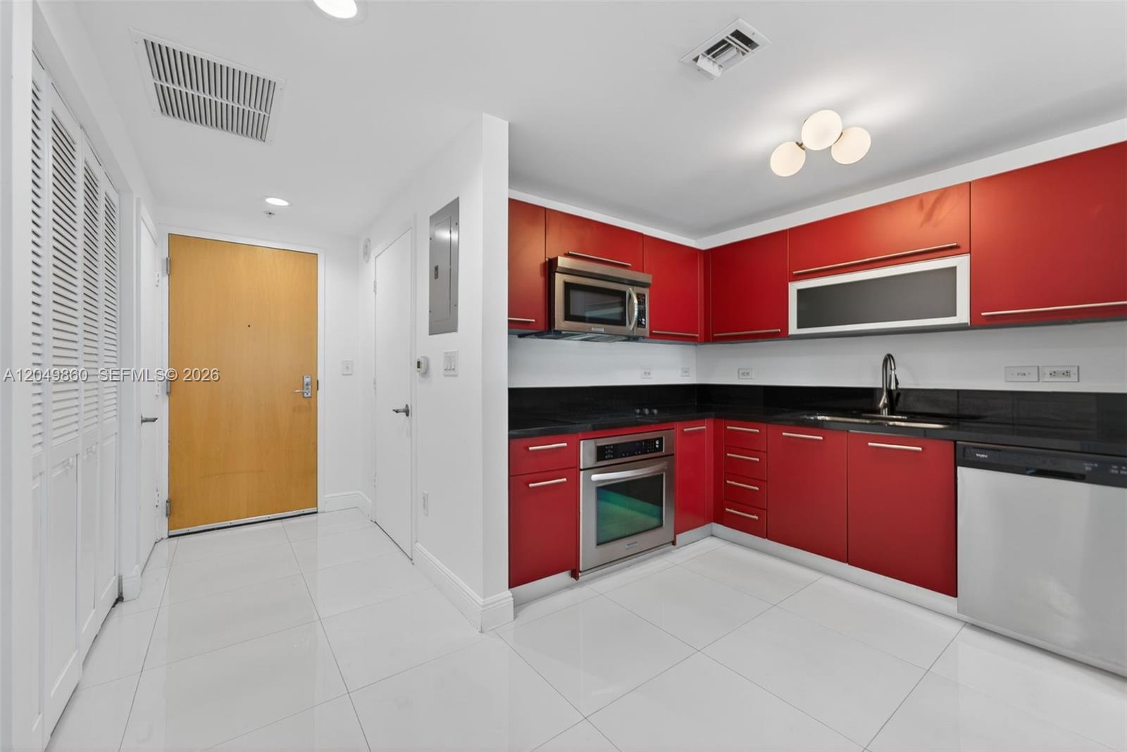 A kitchen features red cabinets, black countertops, stainless steel appliances, and white tile flooring — 253 NE 2nd St # 424, Miami FL 33132, MIAMI, FL