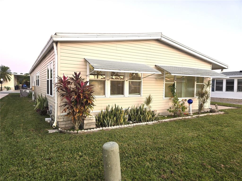 A single-story mobile home with light-colored siding, metal window awnings, and a landscaped yard — 43 LEOPOLD LANE, HAINES CITY, FL