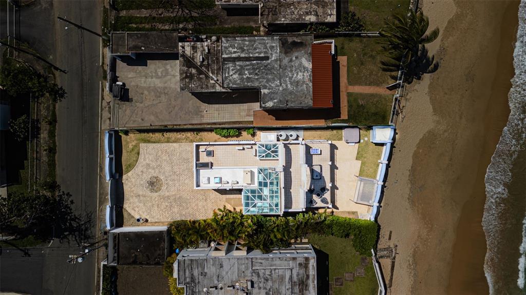 An aerial view shows a beachfront house with a glass-enclosed roof and paved patio area — Carr. 690 LOTE #5 BO. CERRO GORDO, VEGA ALTA, PR