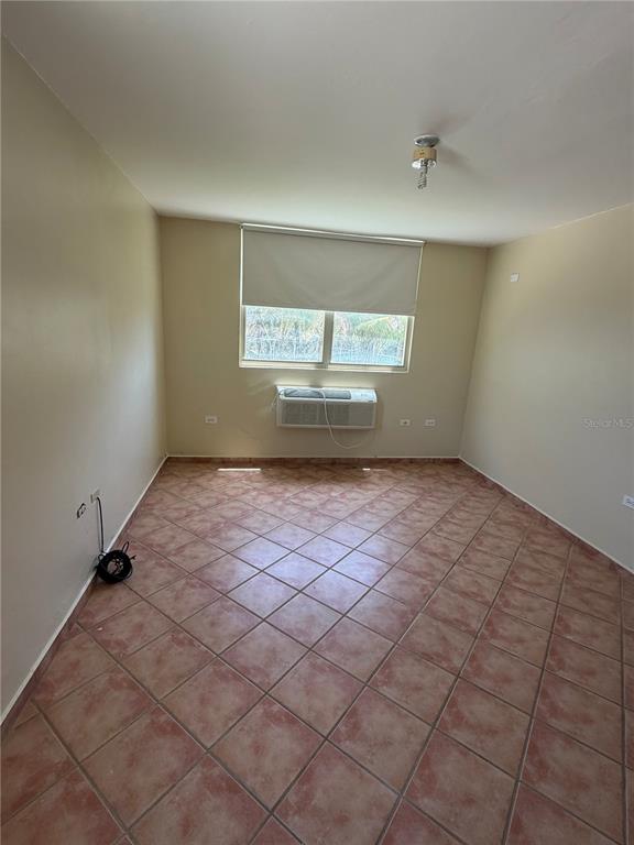 An empty room with beige walls, tile flooring, a window with a shade, and an AC unit — 6690 COND. COVE BY THE SEA UNIT C-201, VEGA ALTA, PR