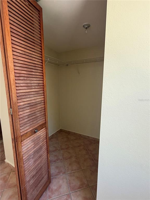 A walk-in closet with louvered wooden doors, tile flooring, and wire shelving — 6690 COND. COVE BY THE SEA UNIT C-201, VEGA ALTA, PR