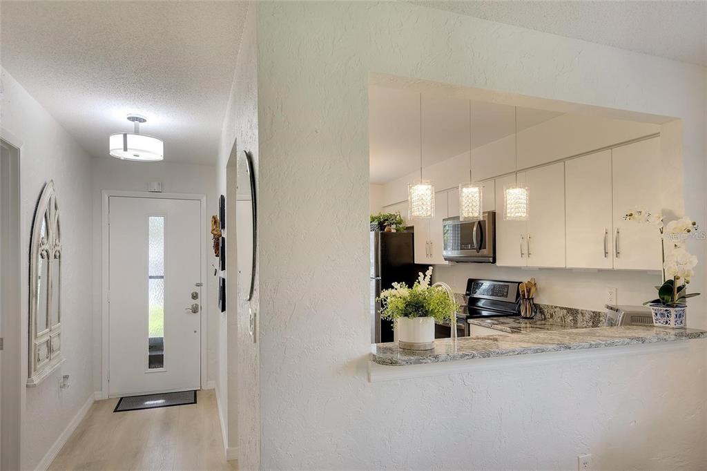 A view from a hallway looking into a kitchen with white cabinets and granite countertops — 6024 28TH STREET W, BRADENTON, FL
