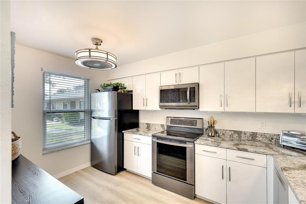 A kitchen features white cabinets, stainless steel appliances, granite countertops, and a ceiling fan light — 6024 28TH STREET W, BRADENTON, FL