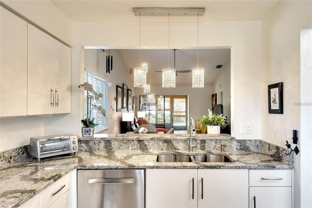 A kitchen with white cabinets, granite countertops, and pendant lights overlooking a living area — 6024 28TH STREET W, BRADENTON, FL