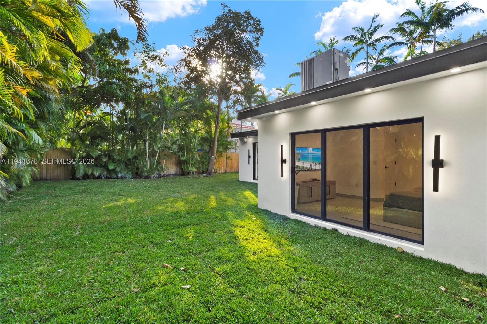 A white exterior wall with sliding glass doors and outdoor lighting overlooks a grassy backyard — 435 W 43rd St, Miami Beach FL 33140, MIAMI BEACH, FL