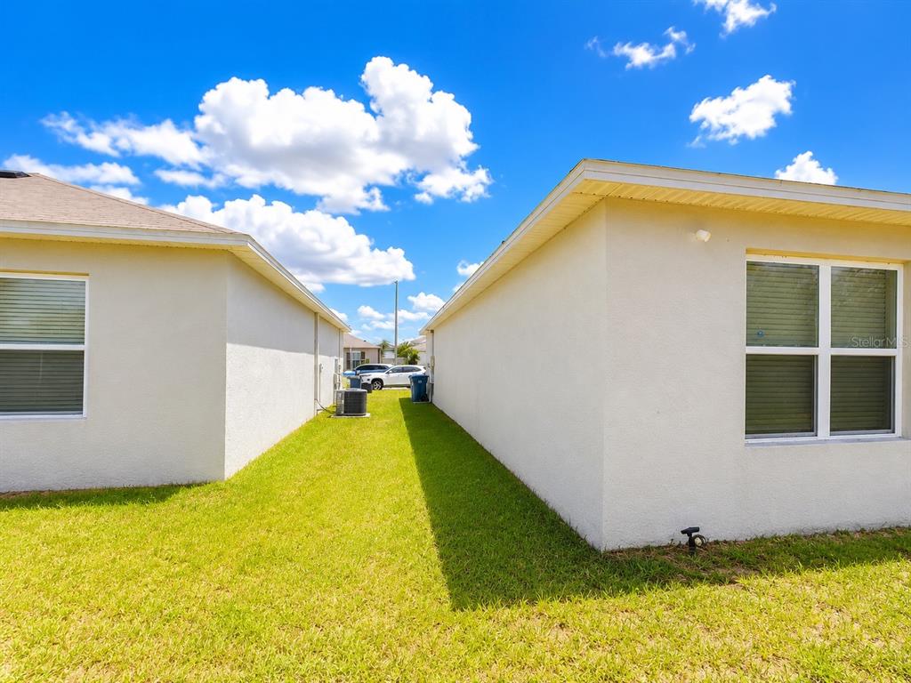 A grassy side yard between two beige stucco houses under a blue sky — 157 HENRY STEVENS DRIVE, HAINES CITY, FL