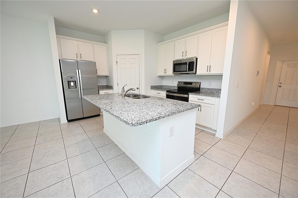 A kitchen features white cabinets, granite countertops, stainless steel appliances, and a central island — 685 CROWN ROSE DRIVE, EAGLE LAKE, FL