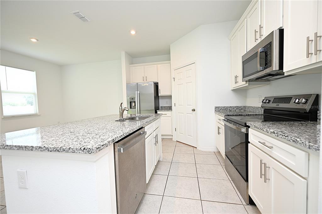 A kitchen features white cabinets, granite countertops, stainless steel appliances, and a central island — 685 CROWN ROSE DRIVE, EAGLE LAKE, FL