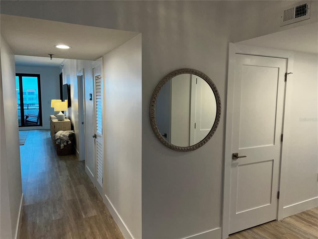 A hallway with light wood-look flooring, a round wall mirror, and white interior doors — 1465 GULF OF MEXICO DRIVE UNIT 504, LONGBOAT KEY, FL
