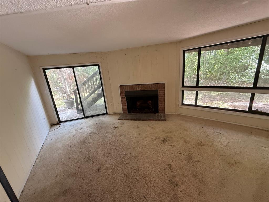 A living room features a brick fireplace, sliding glass doors, and large windows with carpet — 6904 PINETREE LANE E, LAKELAND, FL