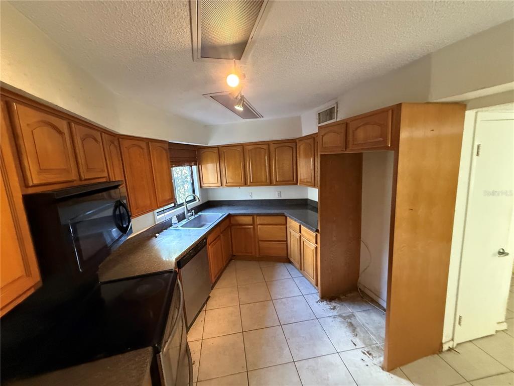 A kitchen with wooden cabinets, dark countertops, tile flooring, and a stainless steel dishwasher — 6904 PINETREE LANE E, LAKELAND, FL