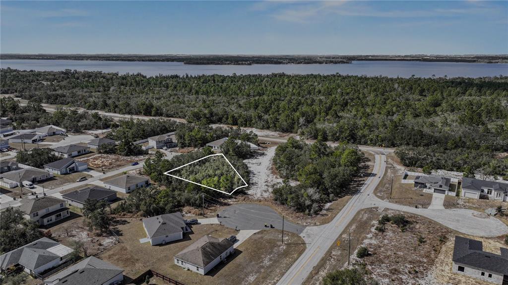 An aerial view shows a vacant, wooded residential lot outlined in white near a lake — 1204 WAVERLY PLACE, POINCIANA, FL