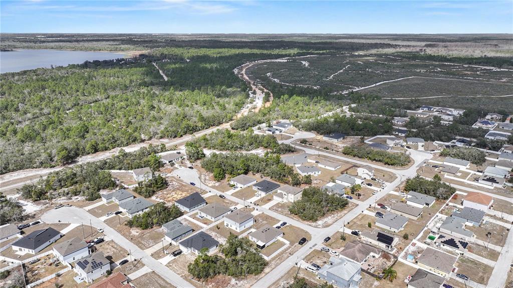 An aerial view shows a suburban neighborhood bordered by a forest and a lake — 1204 WAVERLY PLACE, POINCIANA, FL