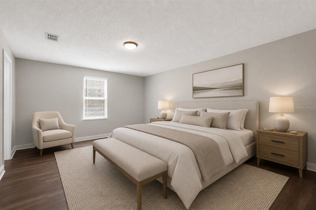A bedroom with a king bed, neutral decor, wood-look flooring, and a small armchair — 3918 PINE BREEZE ROAD S, JACKSONVILLE, FL