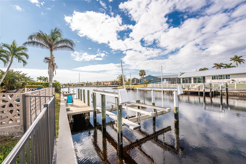 A canal-side boat lift and dock sit beside a residential backyard with palm trees — 951 LASSINO COURT, PUNTA GORDA, FL