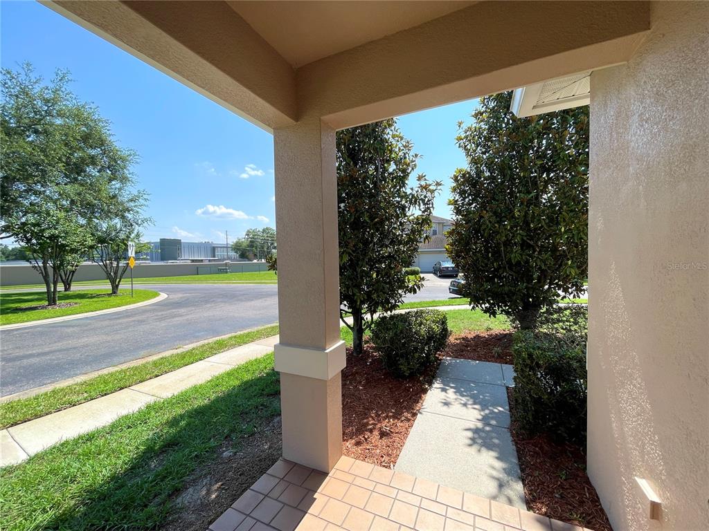 A view from a covered porch looking out toward a street, trees, and houses — 4252 HAWKSLEY PLACE, WESLEY CHAPEL, FL