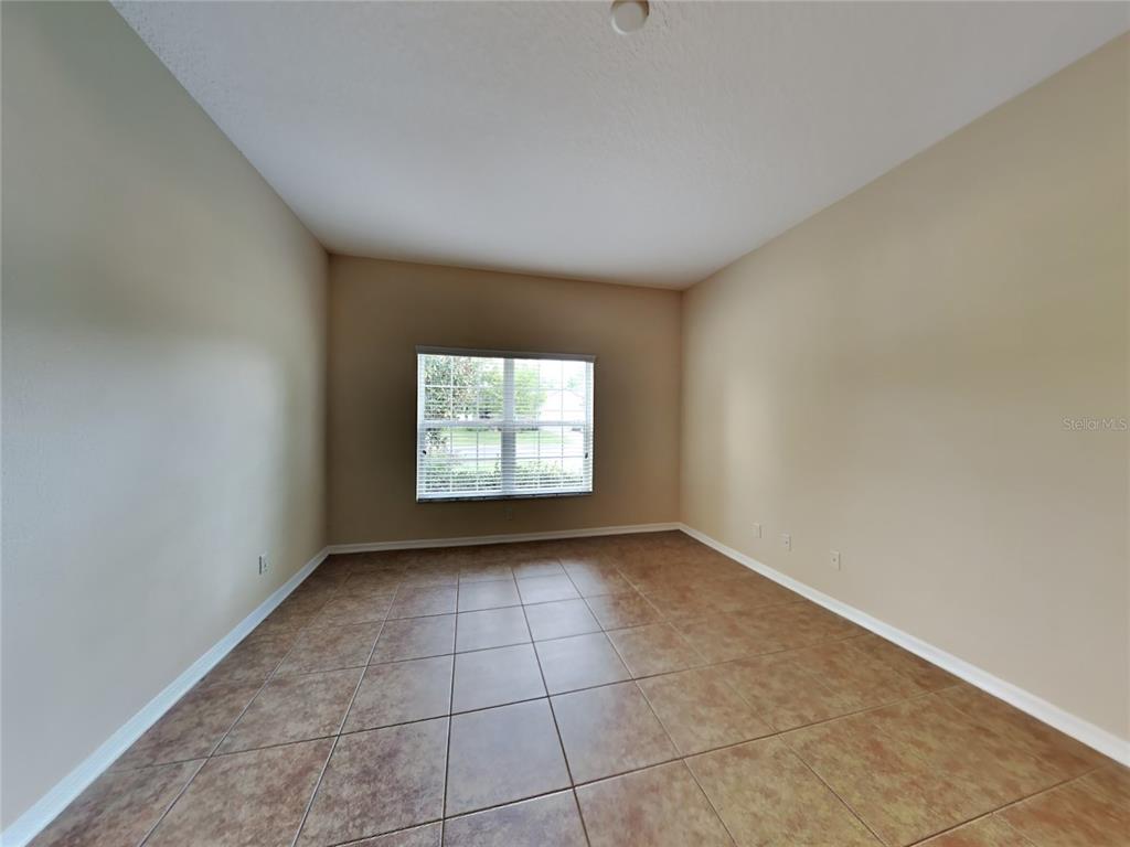An empty room with tan walls, brown tile flooring, and a single window with blinds — 4252 HAWKSLEY PLACE, WESLEY CHAPEL, FL