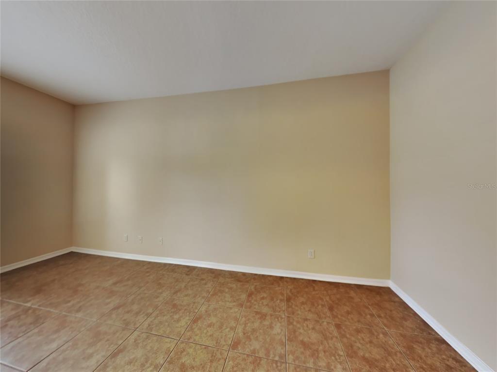 An empty room features beige walls, white baseboards, and brown square floor tiles — 4252 HAWKSLEY PLACE, WESLEY CHAPEL, FL