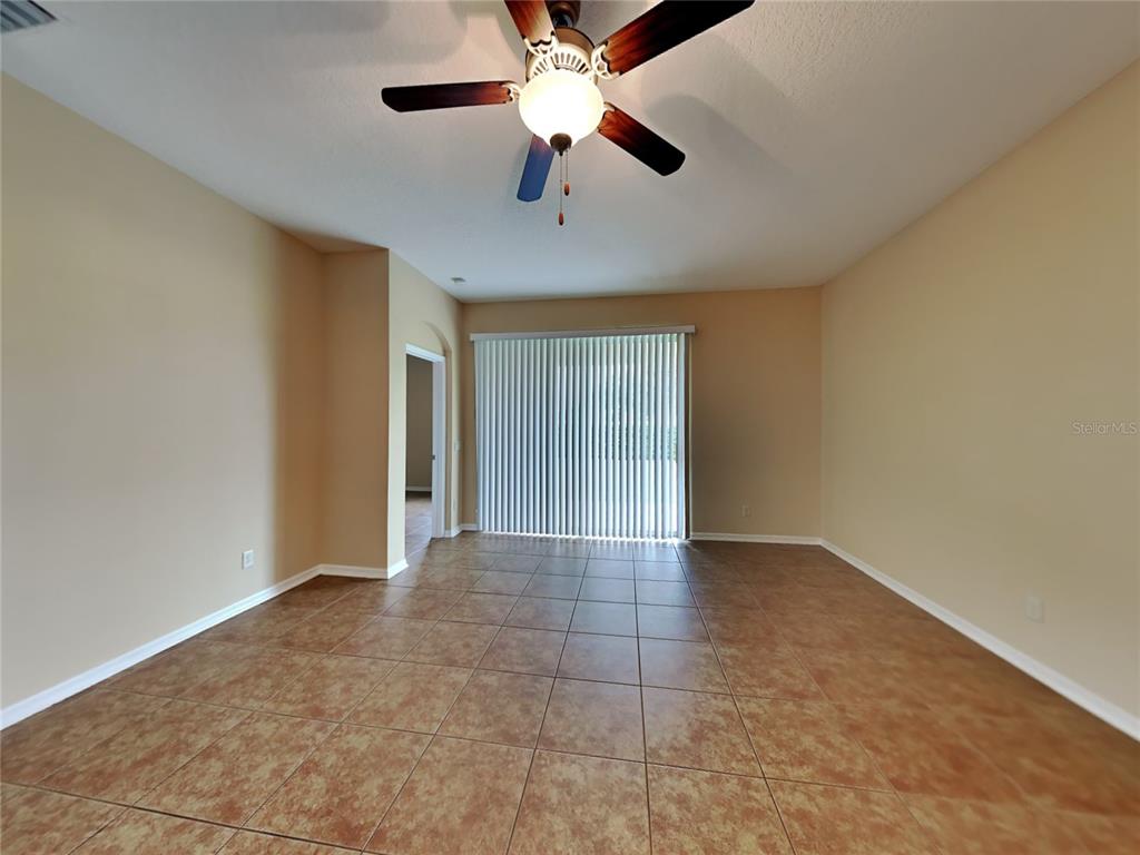 An empty room features tan walls, brown tile flooring, a ceiling fan, and vertical blinds — 4252 HAWKSLEY PLACE, WESLEY CHAPEL, FL