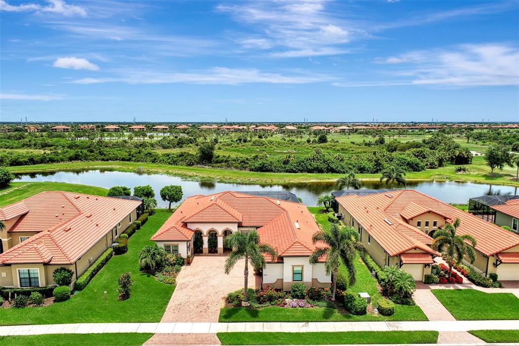 An aerial view shows three suburban houses with orange tile roofs near a pond — 10965 BULLRUSH DRIVE, VENICE, FL