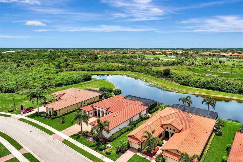 An aerial view shows three houses with orange tile roofs situated along a small lake — 10965 BULLRUSH DRIVE, VENICE, FL