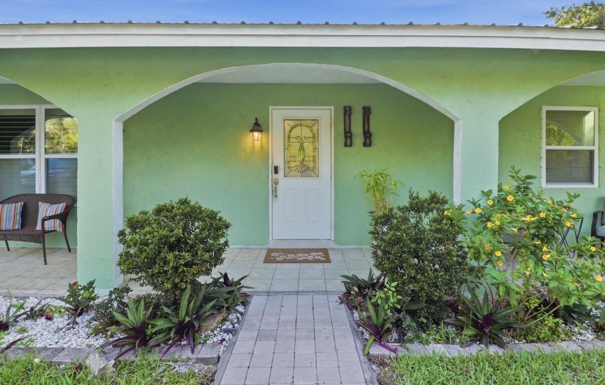 A light green house exterior features a white front door, arched porch, and landscaped walkway — 309 Hach Lane, FL 33415, FL