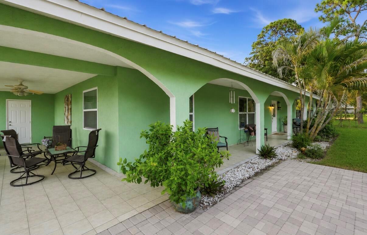 A green house exterior features a covered patio with arched columns and paved flooring — 309 Hach Lane, FL 33415, FL