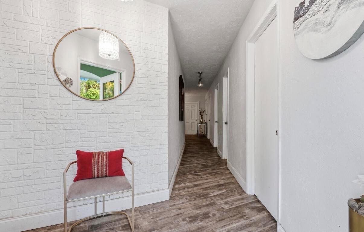 A hallway features white brick-patterned walls, wood-look flooring, a round mirror, and a small chair — 309 Hach Lane, FL 33415, FL