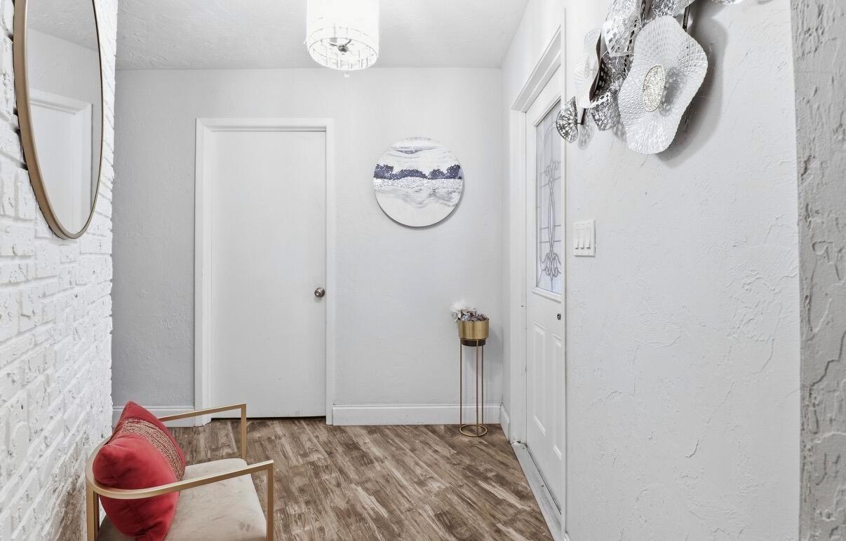 A bright entryway features wood-look flooring, a white brick wall, a red chair, and decor — 309 Hach Lane, FL 33415, FL