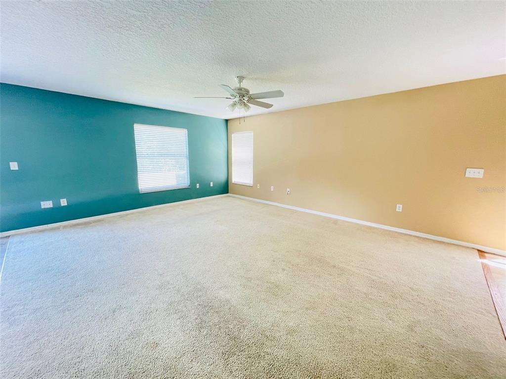 An empty room features beige carpet, a ceiling fan, and walls painted teal and tan — 155 OWENSHIRE CIRCLE, KISSIMMEE, FL
