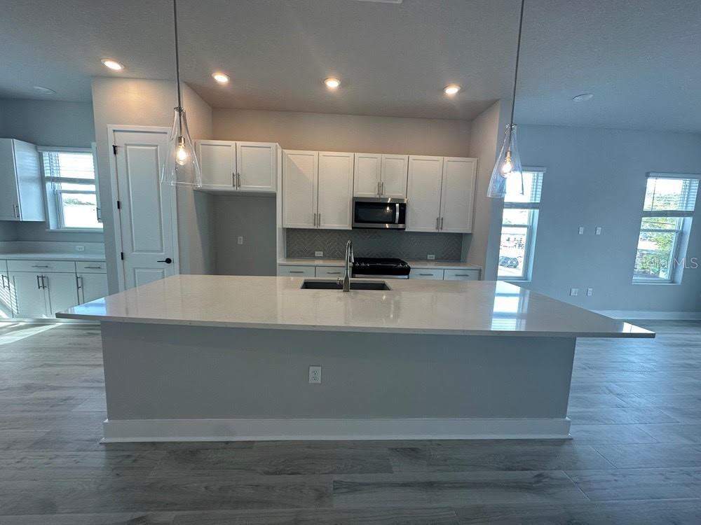 A modern kitchen features white cabinets, a large quartz island, and light wood-look flooring — 89 28TH STREET S, ST PETERSBURG, FL