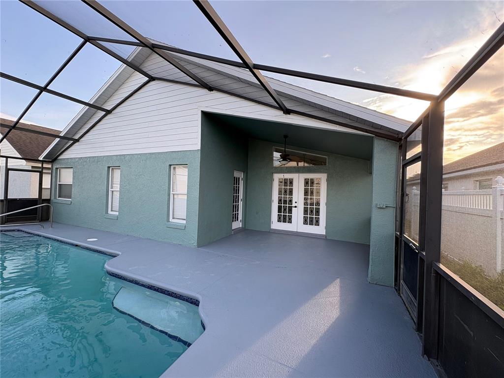 A covered patio with a pool, gray flooring, and white French doors under a screen enclosure — 11215 CRYSTAL GLEN BOULEVARD, ORLANDO, FL