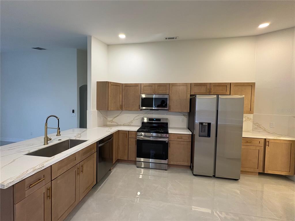A modern kitchen features light wood cabinets, white marble-patterned countertops, and stainless steel appliances — 11215 CRYSTAL GLEN BOULEVARD, ORLANDO, FL