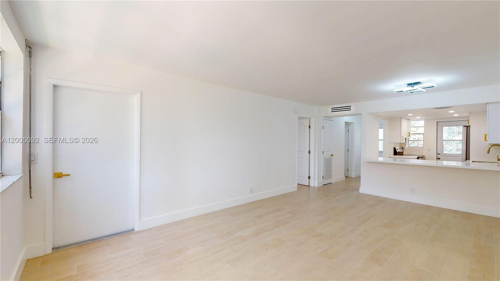 A bright, empty living room features light-colored tile flooring, white walls, and an open kitchen — 1333 E Hallandale Beach Blvd # 326, Hallandale Beach FL 33009, HALLANDALE BEACH, FL