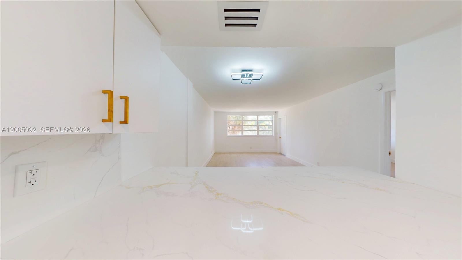 A white kitchen counter with marble-style veining overlooks a bright, empty living area — 1333 E Hallandale Beach Blvd # 326, Hallandale Beach FL 33009, HALLANDALE BEACH, FL