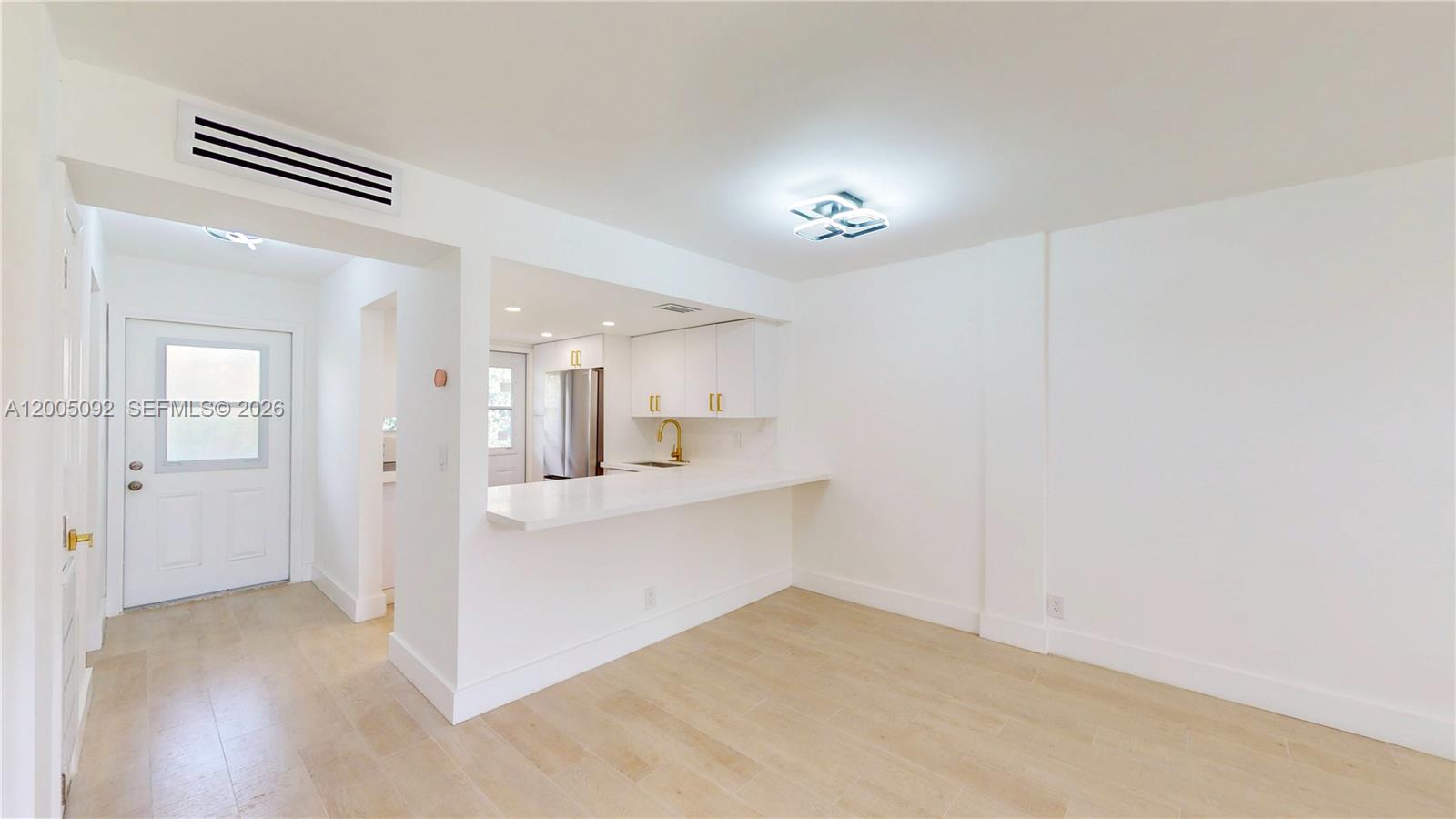 A bright, minimalist room features light wood flooring, white walls, and an open kitchen pass-through — 1333 E Hallandale Beach Blvd # 326, Hallandale Beach FL 33009, HALLANDALE BEACH, FL