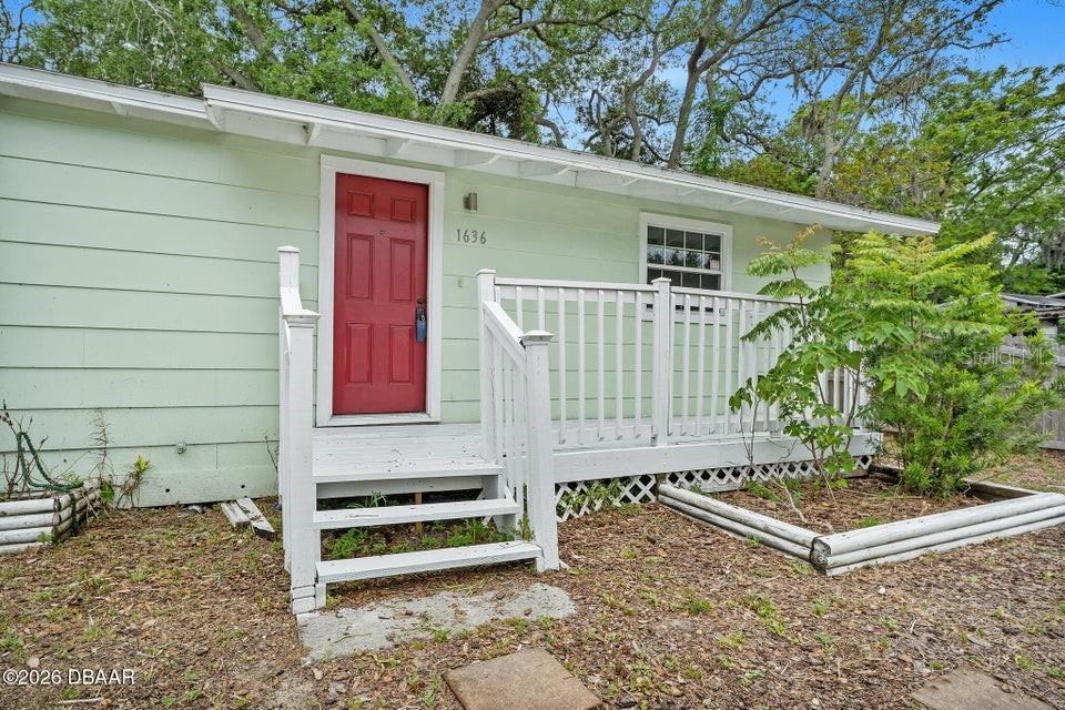A light green house exterior features a red front door and a white wooden deck — 1636 VALENCIA AVENUE, DAYTONA BEACH, FL