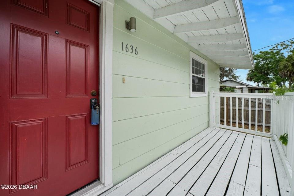 A red front door opens onto a white wooden porch with light green siding — 1636 VALENCIA AVENUE, DAYTONA BEACH, FL