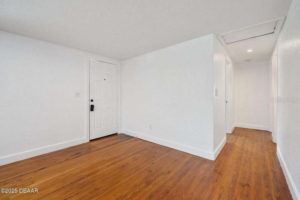 An empty room features white walls, hardwood flooring, and a white front door — 1636 VALENCIA AVENUE, DAYTONA BEACH, FL