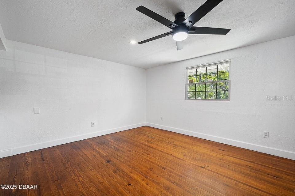 An empty room features white walls, dark wood flooring, and a ceiling fan with light — 1636 VALENCIA AVENUE, DAYTONA BEACH, FL
