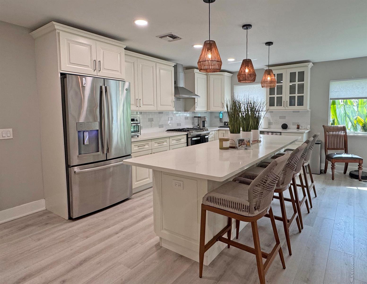 A modern kitchen features white cabinetry, a large quartz island with barstools, and pendant lighting — 106 Periwinkle Drive, Hypoluxo FL 33462, HYPOLUXO, FL