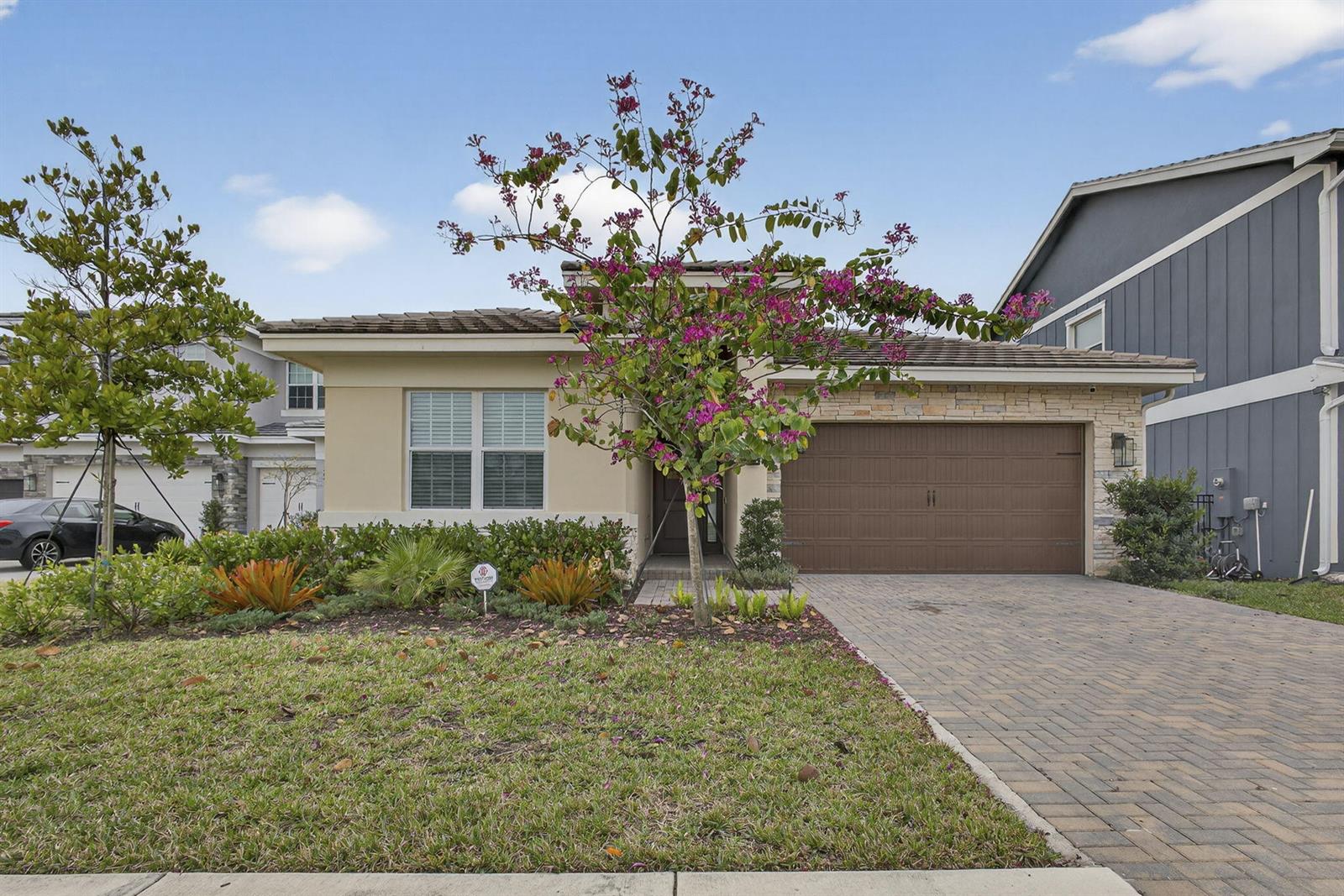 A single-story house with a paved driveway, a brown garage door, and a flowering tree — 1411 Thistle Place, Loxahatchee FL 33470, LOXAHATCHEE, FL